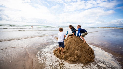 Children climb a mound of sand on Rhosili beach, Gower, Wales